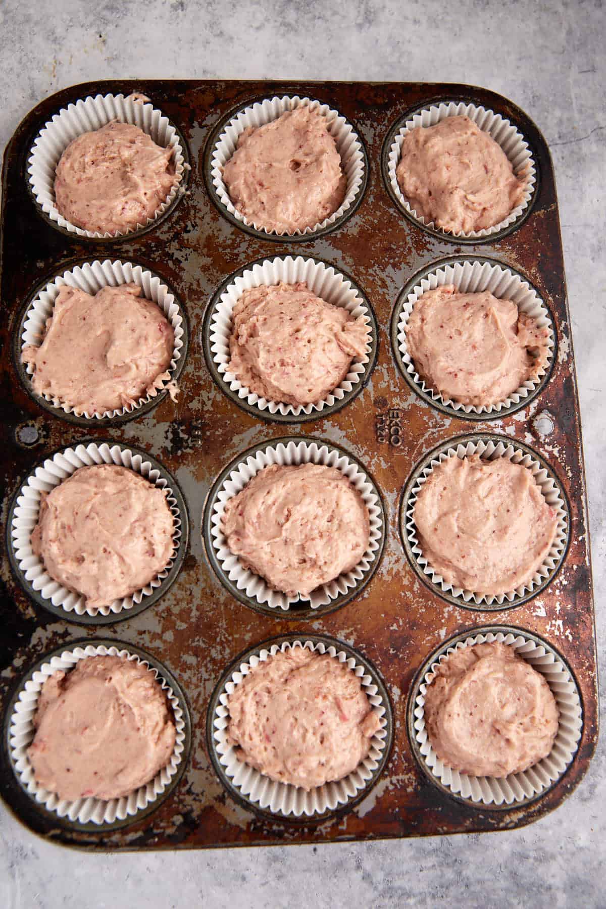 Strawberry cupcake batter in paper liners in a muffin tin.