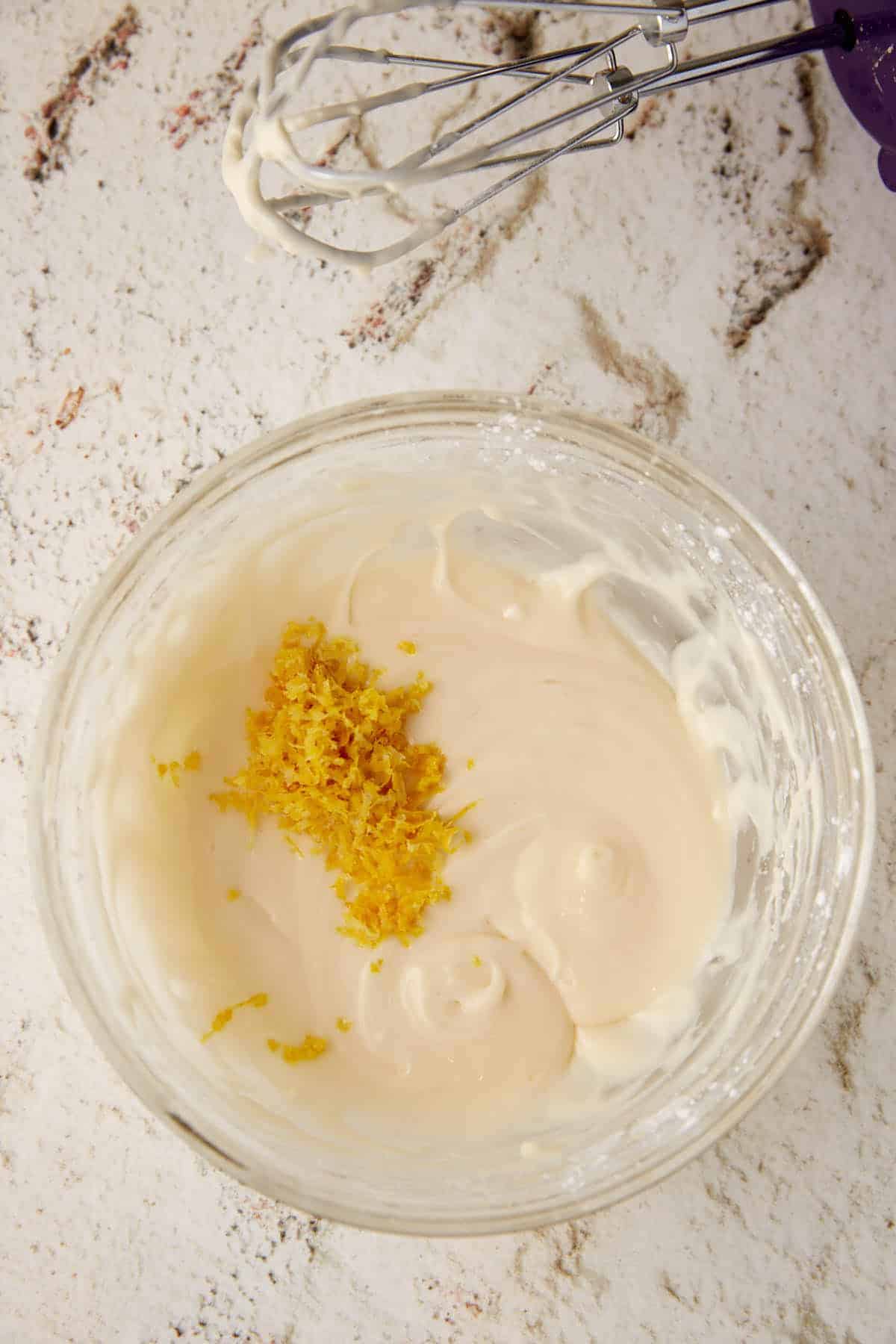 Lemon zest on top of a lemon glaze in a bowl.