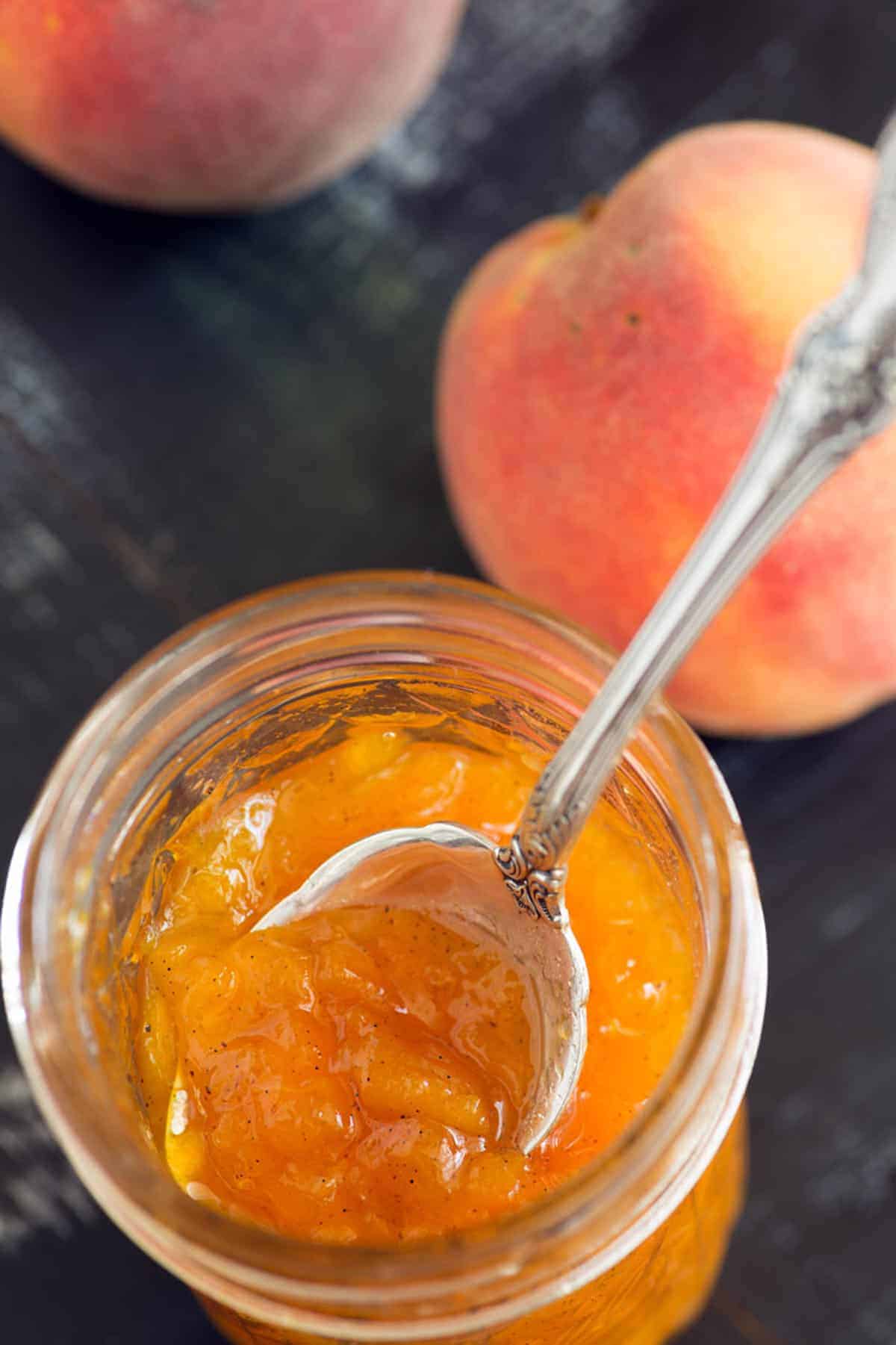 A jar of peach jam with a serving spoon in the top.