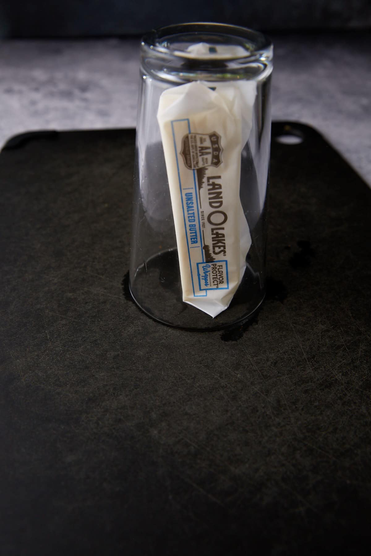 A stick of butter underneath a glass.
