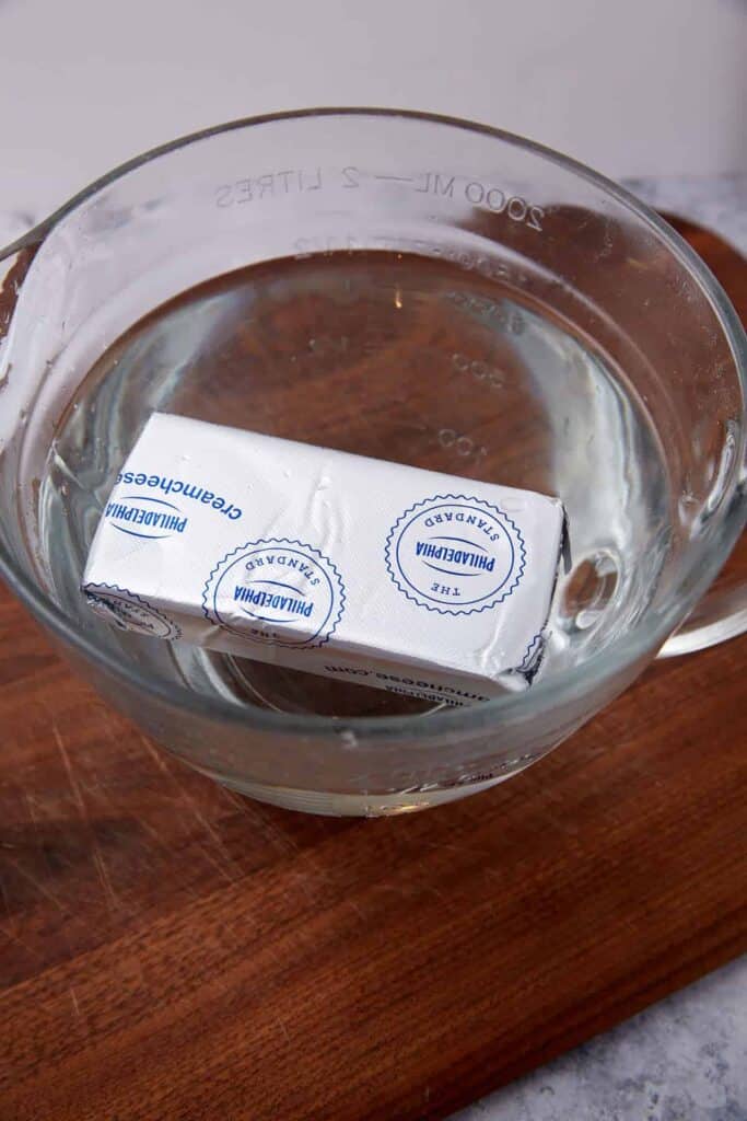 A block of cream cheese in a bowl of hot water.