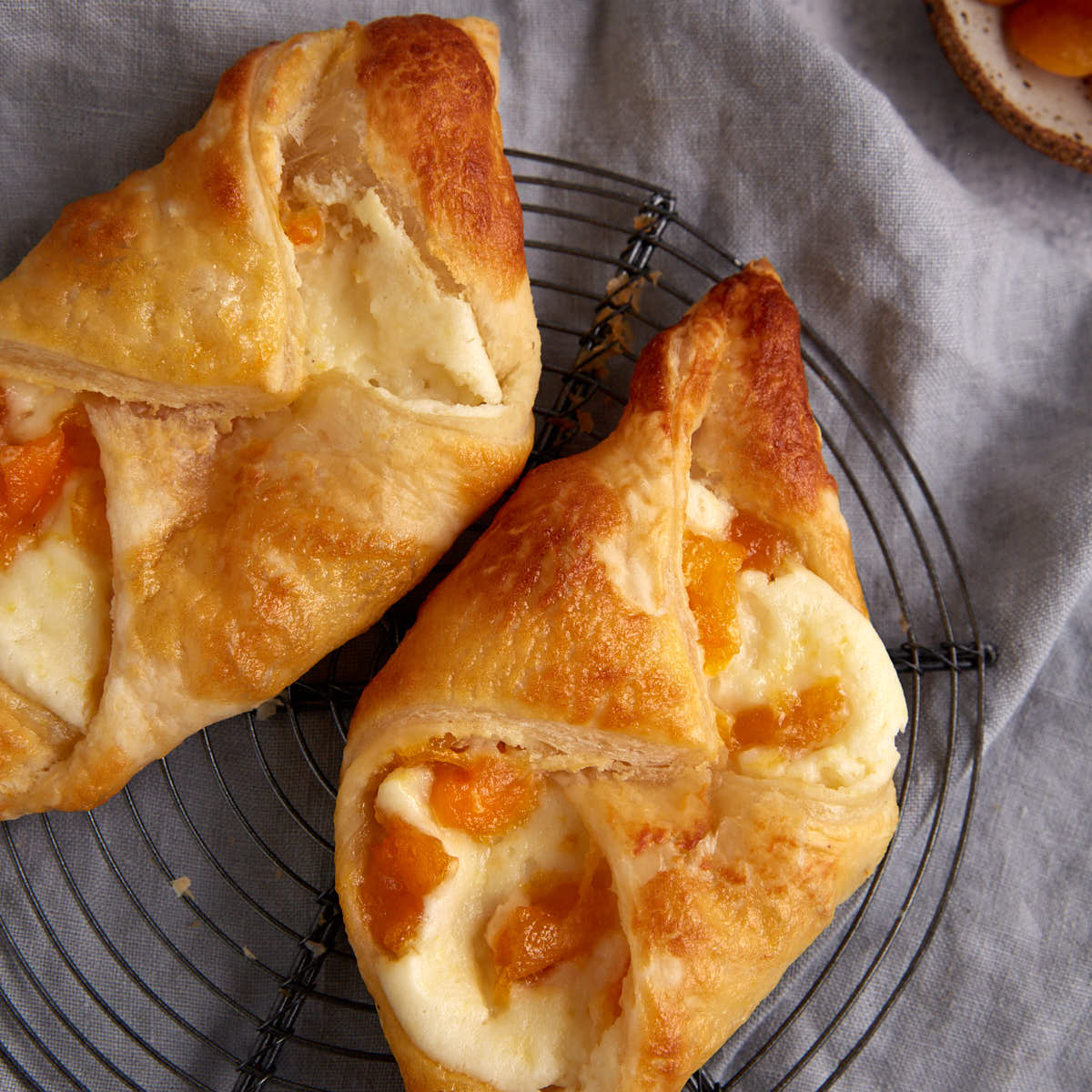 Two cream cheese pastries with apricots on a cooling rack.
