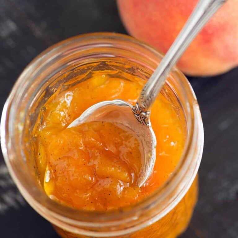 A jar of peach jam with a spoon in the top.