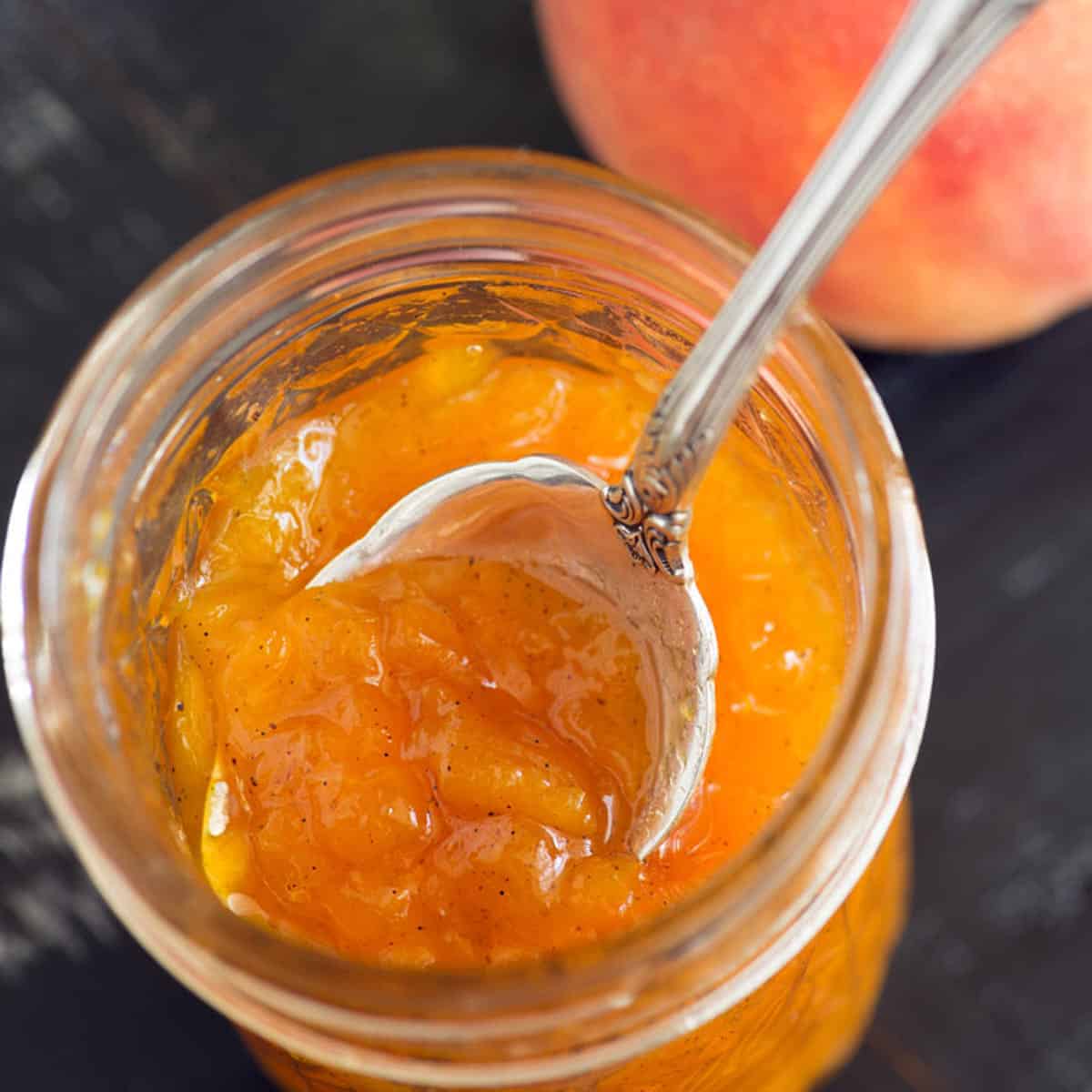A jar of peach jam with a spoon in the top.