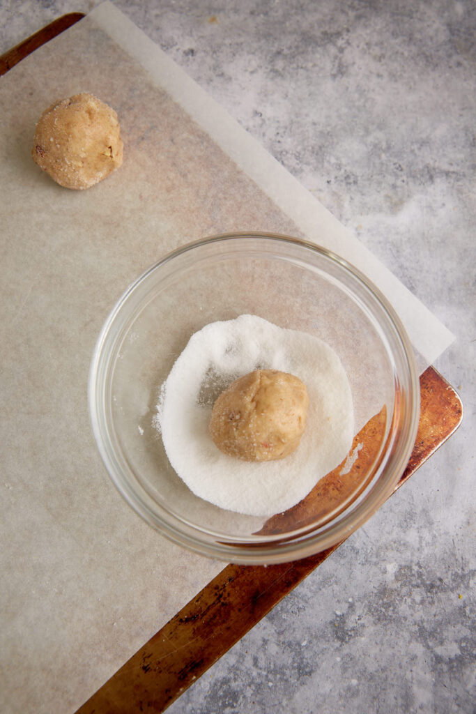 A ball of cookie dough in a bowl of sugar.