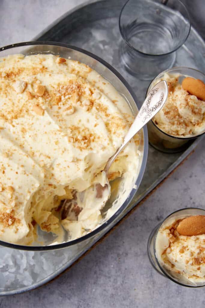 A bowl of banana pudding with a spoon in it next to two servings.