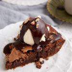 A slice of brownie pie topped with ice cream and chocolate syrup.