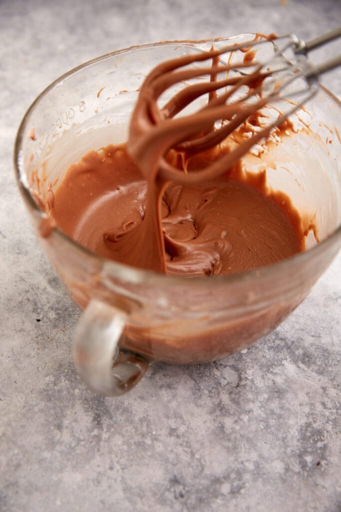 Chocolate frosting in a bowl with a hand mixer.