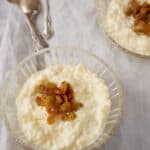 Two glass bowls of custard rice pudding topped with raisins.