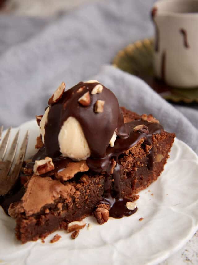 A slice of chocolate brownie pie topped with ice cream and syrup.