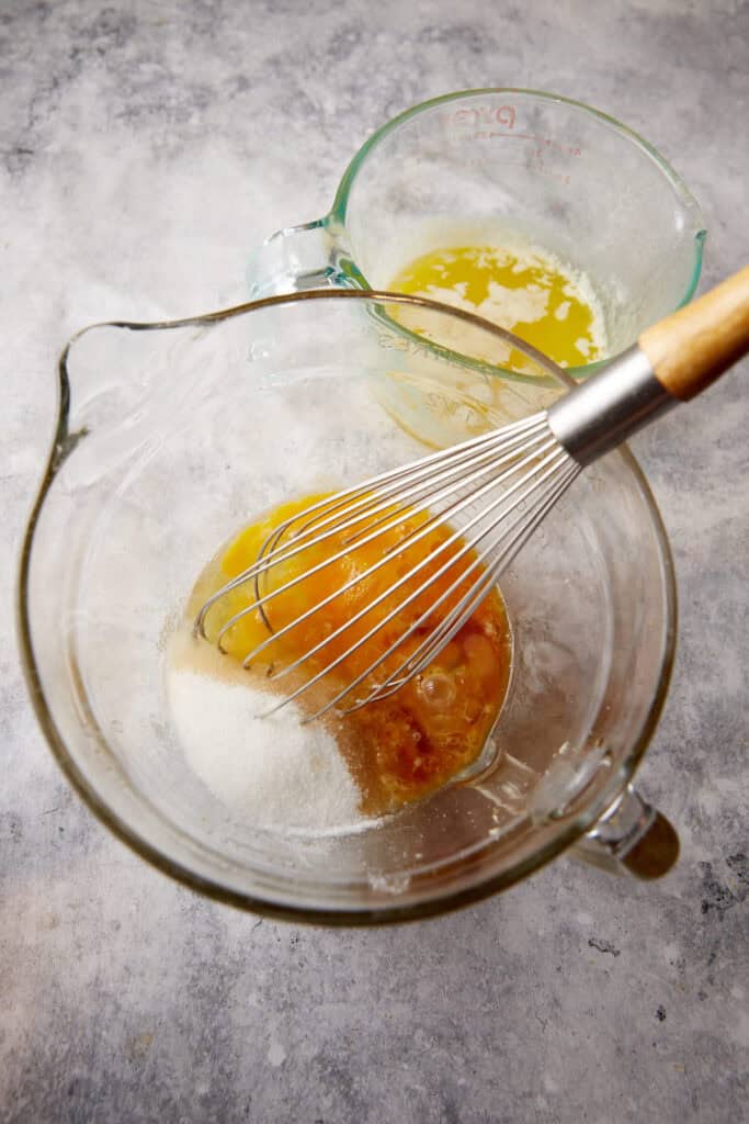 a bowl of eggs, sugar and butter with a whisk. 