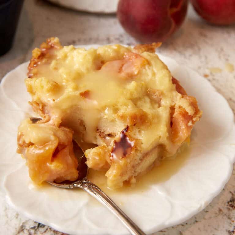 A serving of peach bread pudding on a plate with a fork.