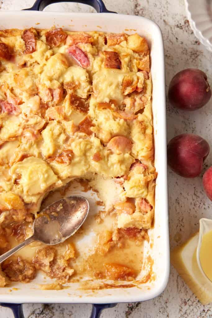 A casserole dish with peach bread pudding with part of it removed.