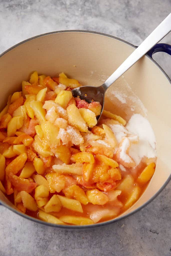 A dutch oven with fresh peaches and sugar.