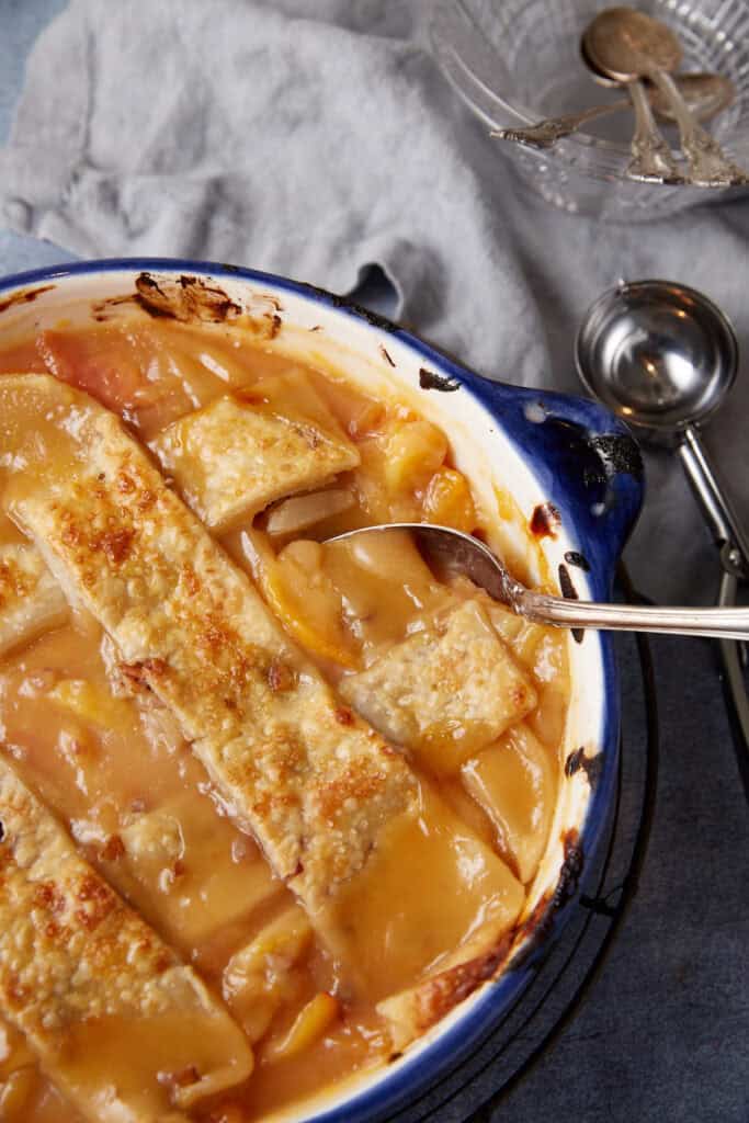 A casserole dish of a baked peach cobbler with pie crusts.