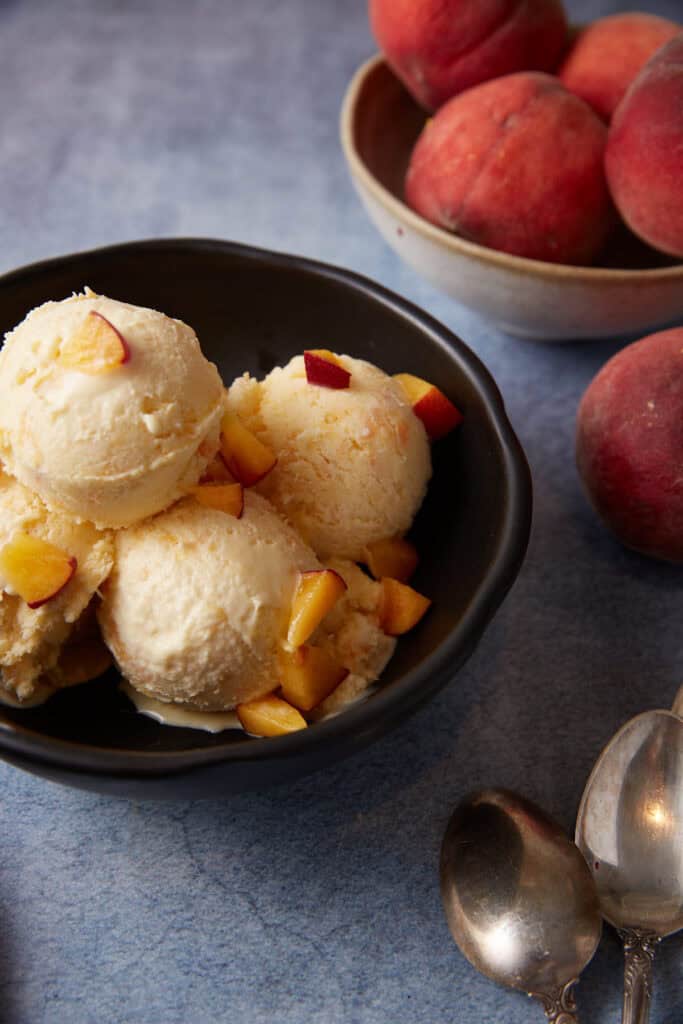 Peach ice cream in a bowl with peach chunks on top.