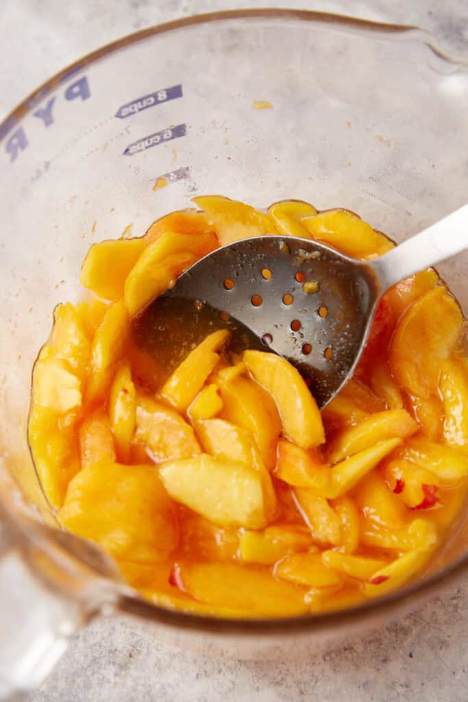 A bowl of sliced peaches that have formed juice in a bowl.