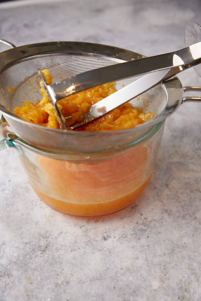 Peaches being mashed in a wire sieve.
