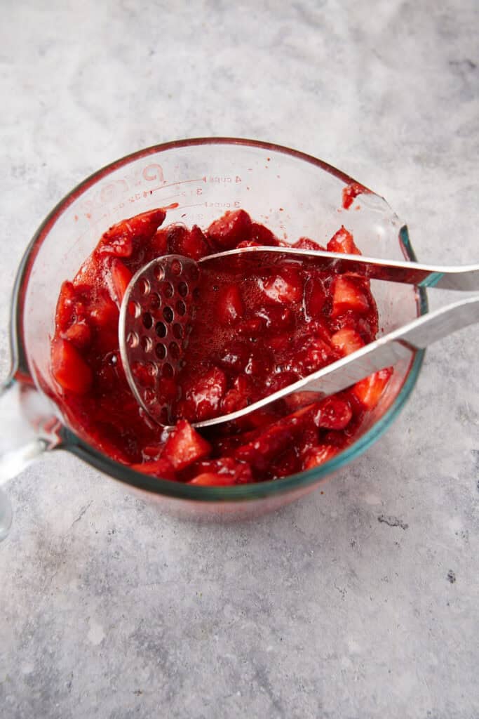 Strawberries being mashed with a potato masher.