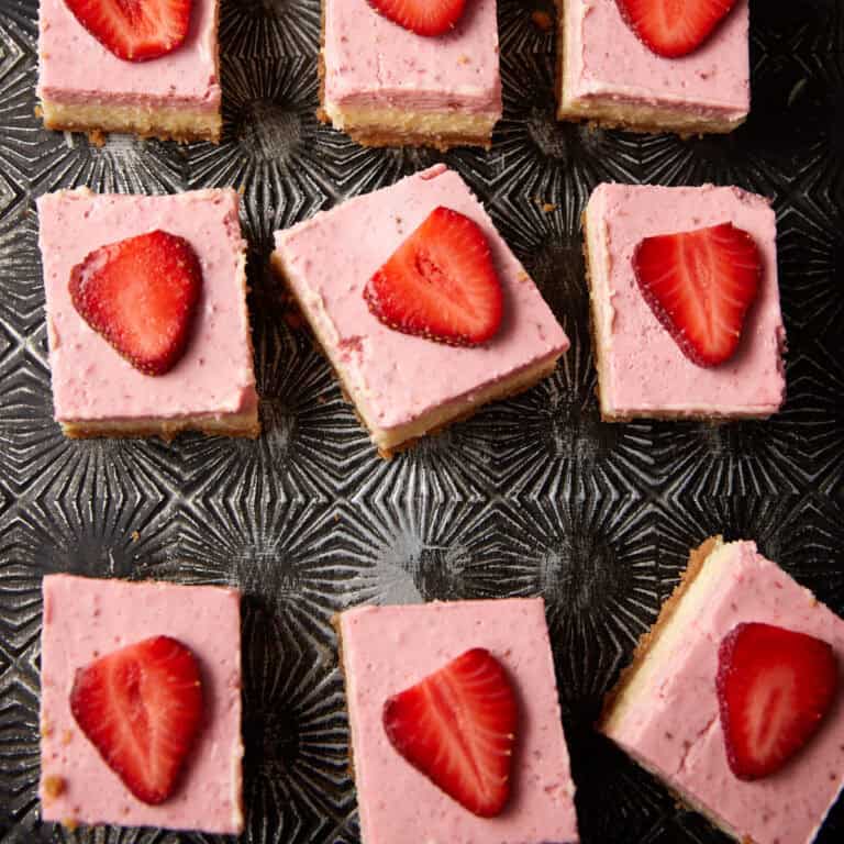 Strawberry cheesecake bars line up on a tray.