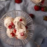 A glass bowl of strawberry ice cream with a spoon.