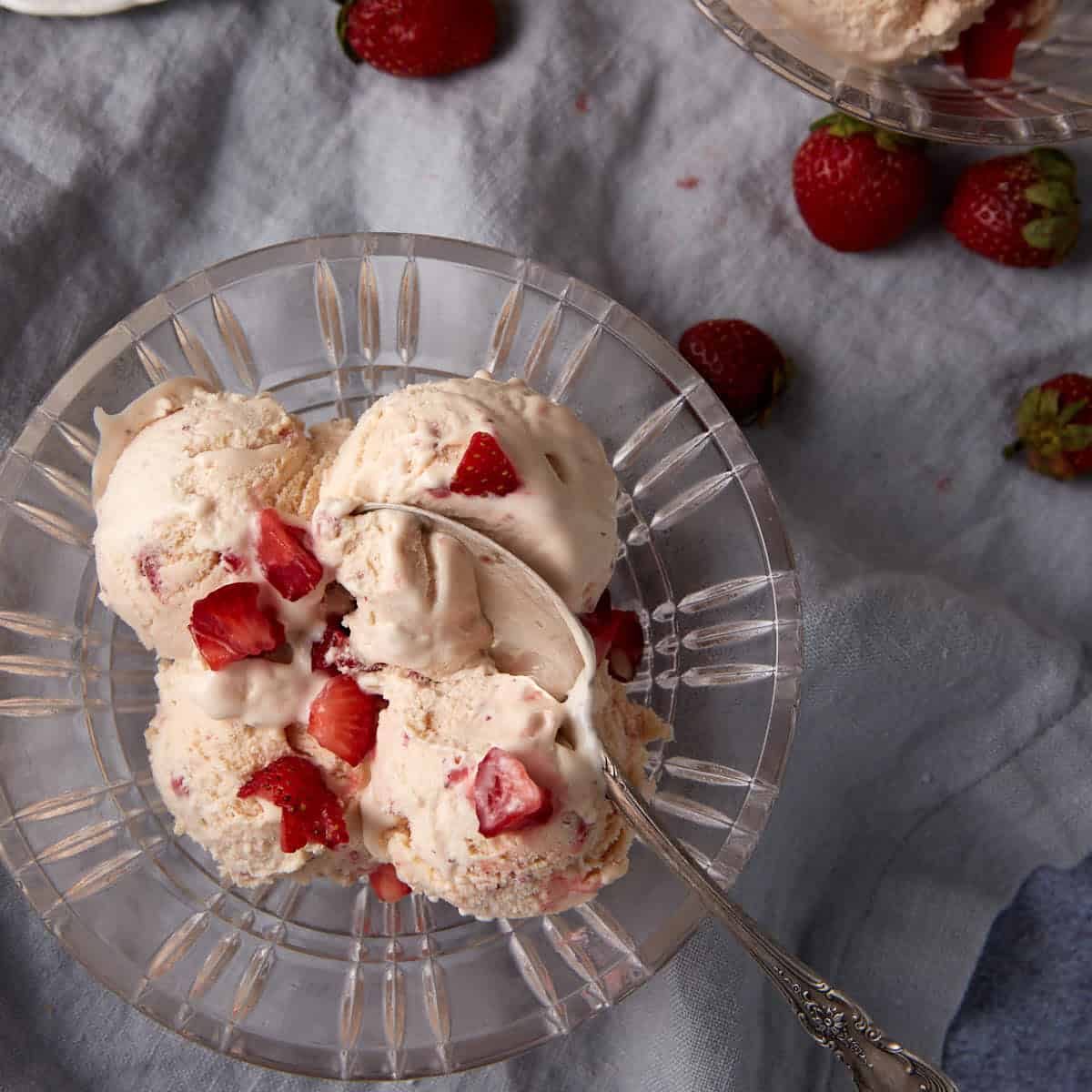 A glass bowl of strawberry ice cream with a spoon.