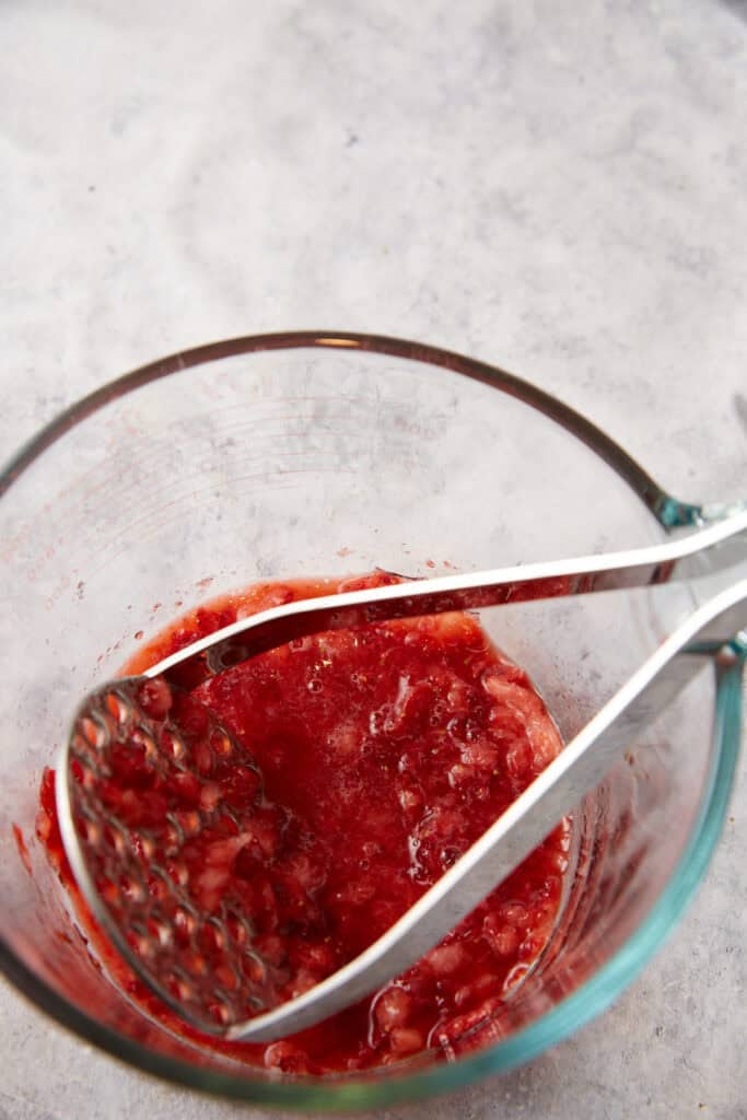 A potato masher mashing strawberries.
