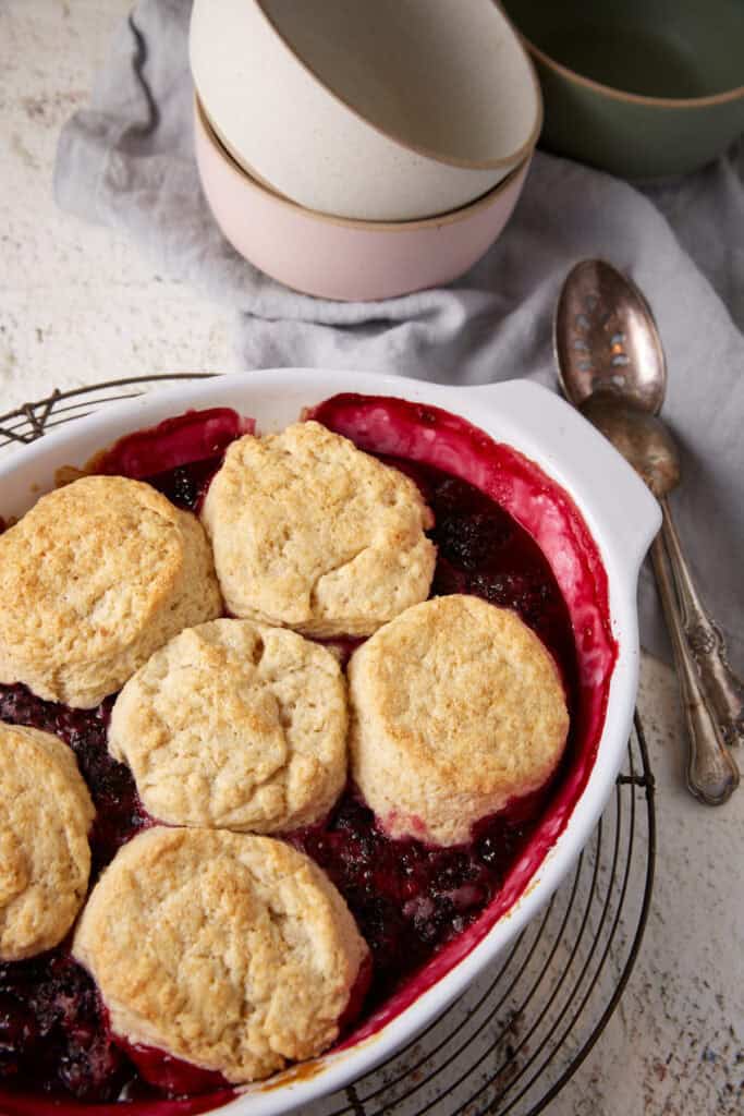 A baking dish with blackberry cobbler next to serving bowls.