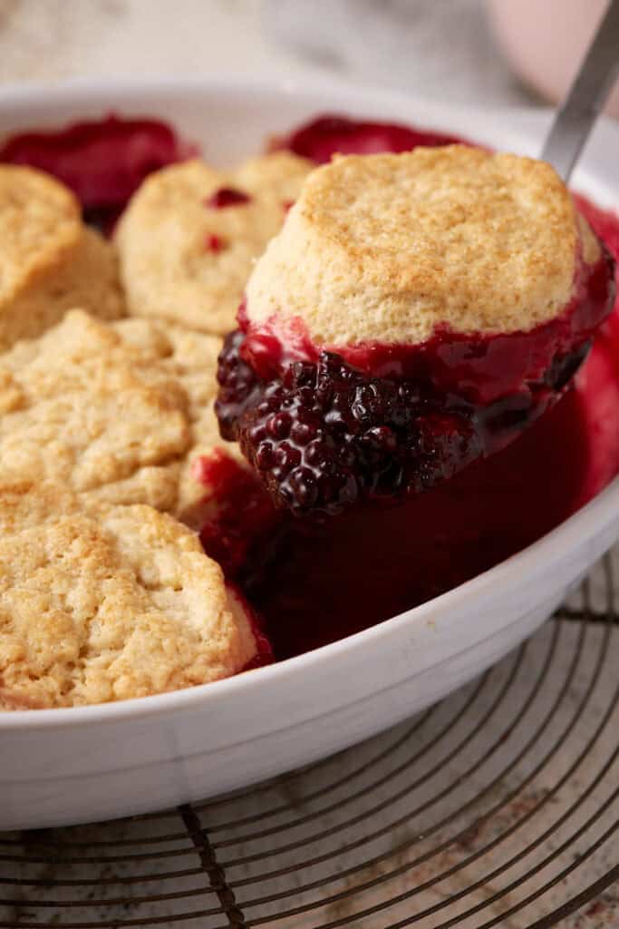 A spoon lifting blackberry cobbler out of a dish.