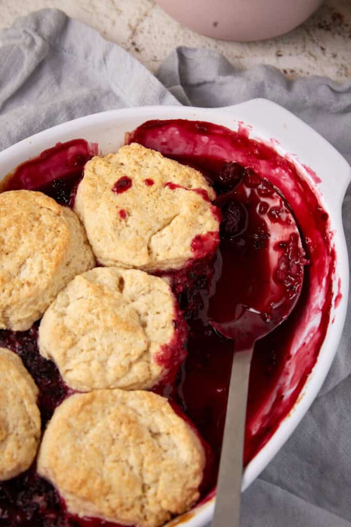 A casserole dish of blackberry cobbler with a serving spoon.