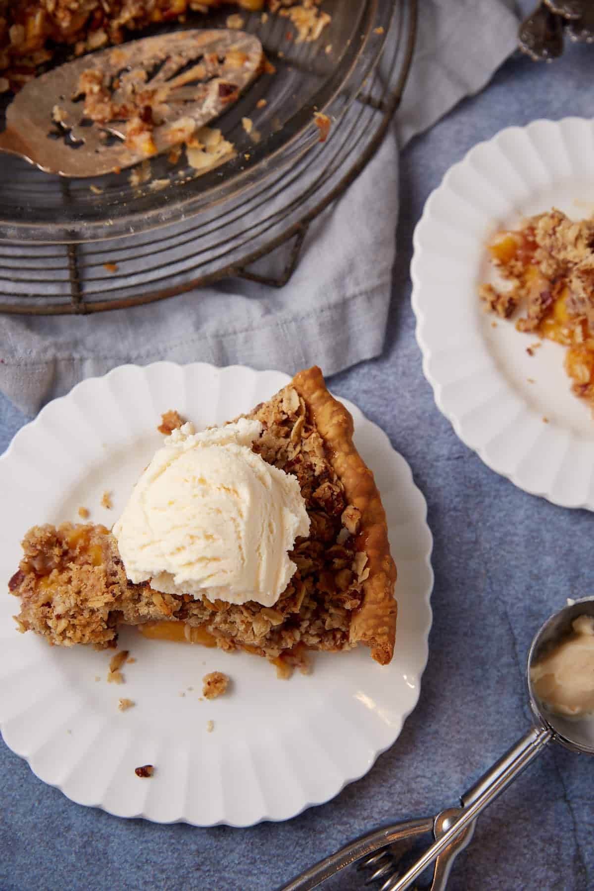 A slice of peach pie with crumble on a plate with ice cream.