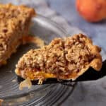 A slice of peach pie with crumble topping.