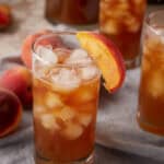 A glass of peach tea over ice in a glass.