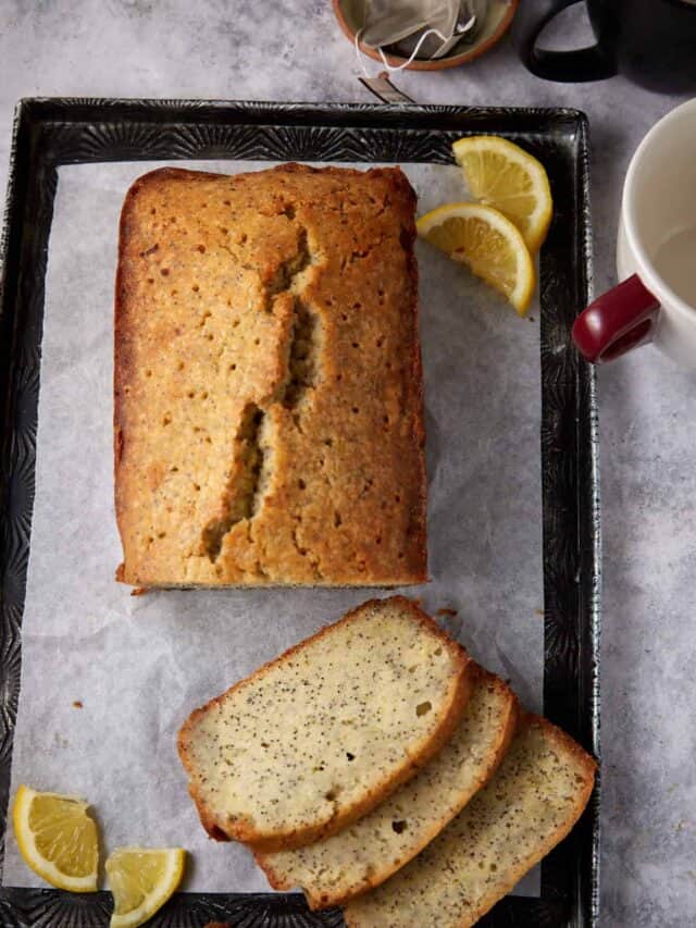 A sliced loaf of lemon poppy seed cake next to a cup.