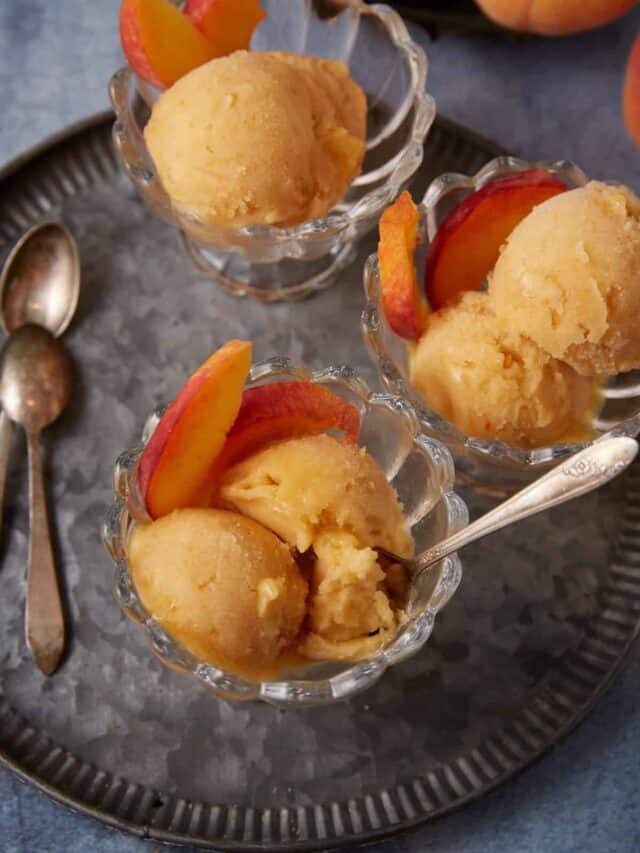 A spoon dipping out some peach sorbet from a glass bowl.