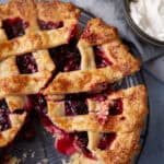 A cut blackberry pie next to whipped cream.