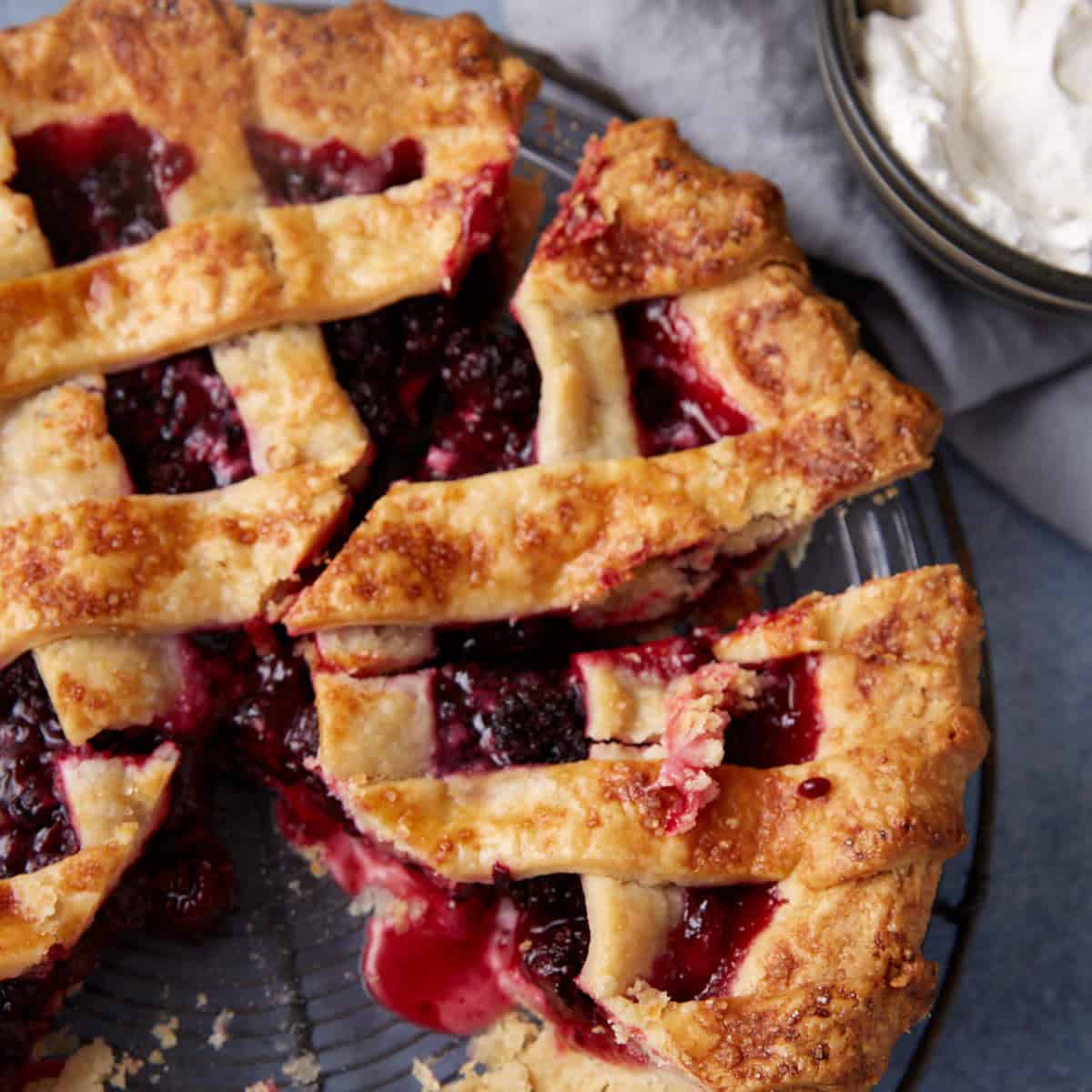 A cut blackberry pie next to whipped cream.