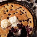 An iron skillet with a blackberry cobbler topped with ice cream.