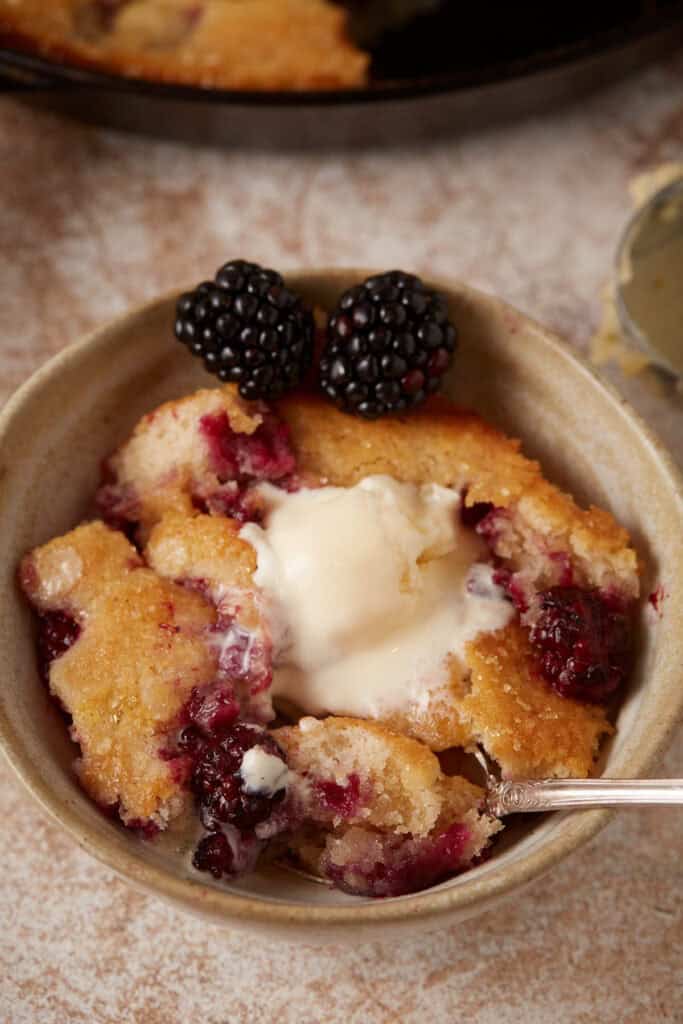 Blackberry skillet cobbler in a bowl with a spoon. ,