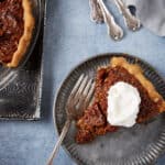 A slice of chocolate bourbon pecan pie with whipped cream on top.