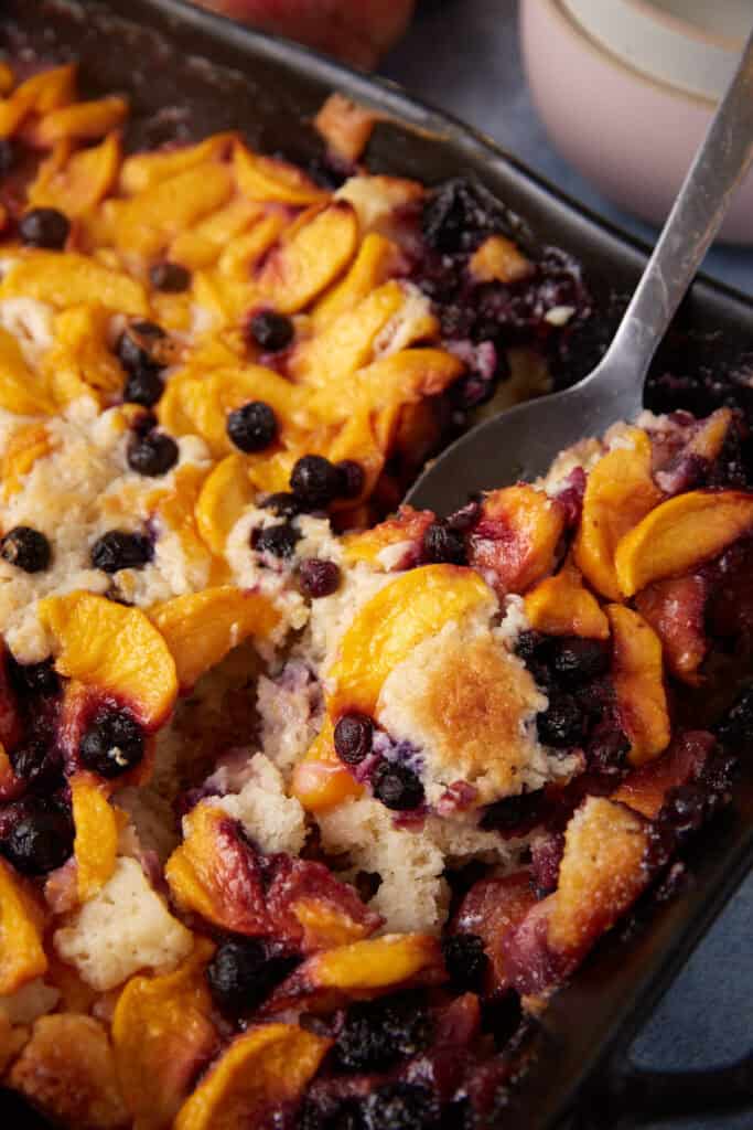 A spoon scooping out peach blueberry cobbler.