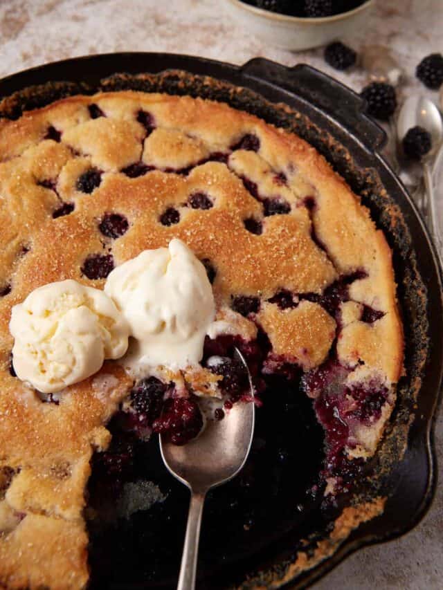 Blackberry cobbler topped with ice cream in an iron skillet.