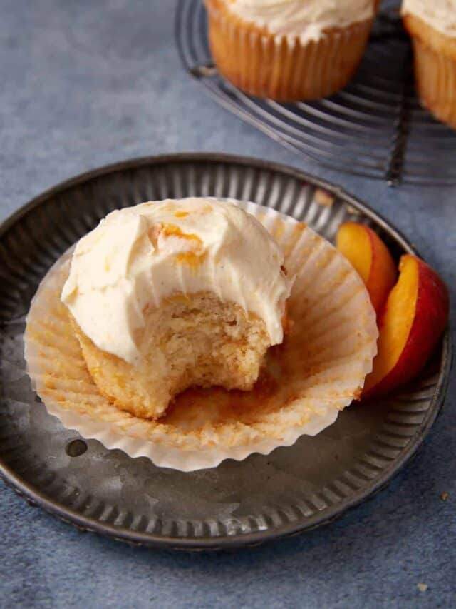 A single peach cupcake with a bite taken out of it.