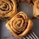 A baked apple cinnamon roll being removed from a pan.