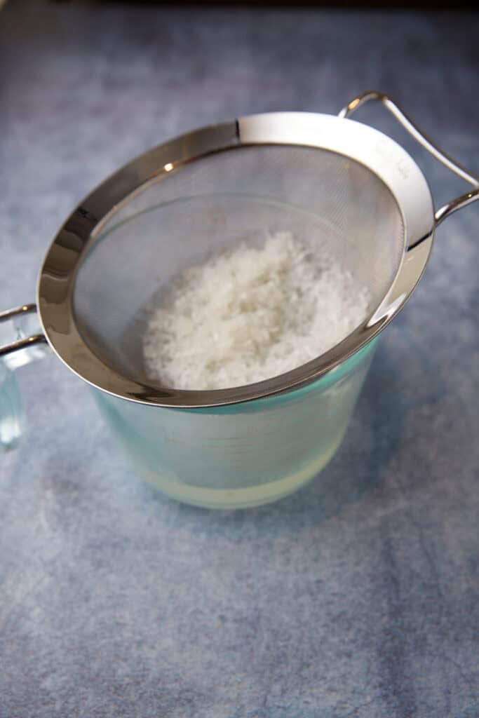 Coconut being strained out of coconut syrup.