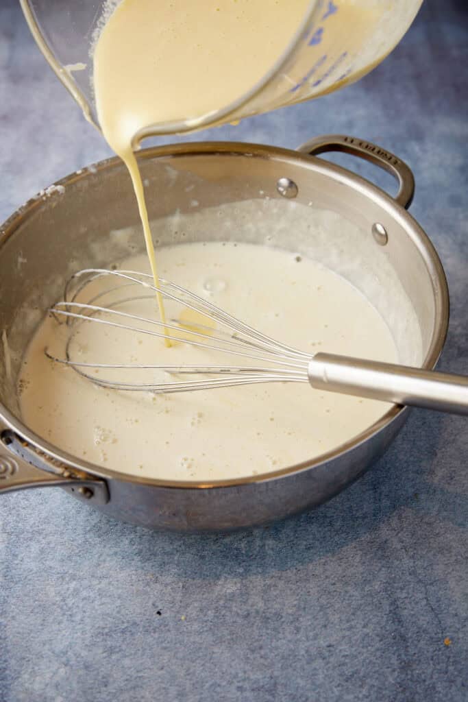 Tempered eggs being poured into warm milk.