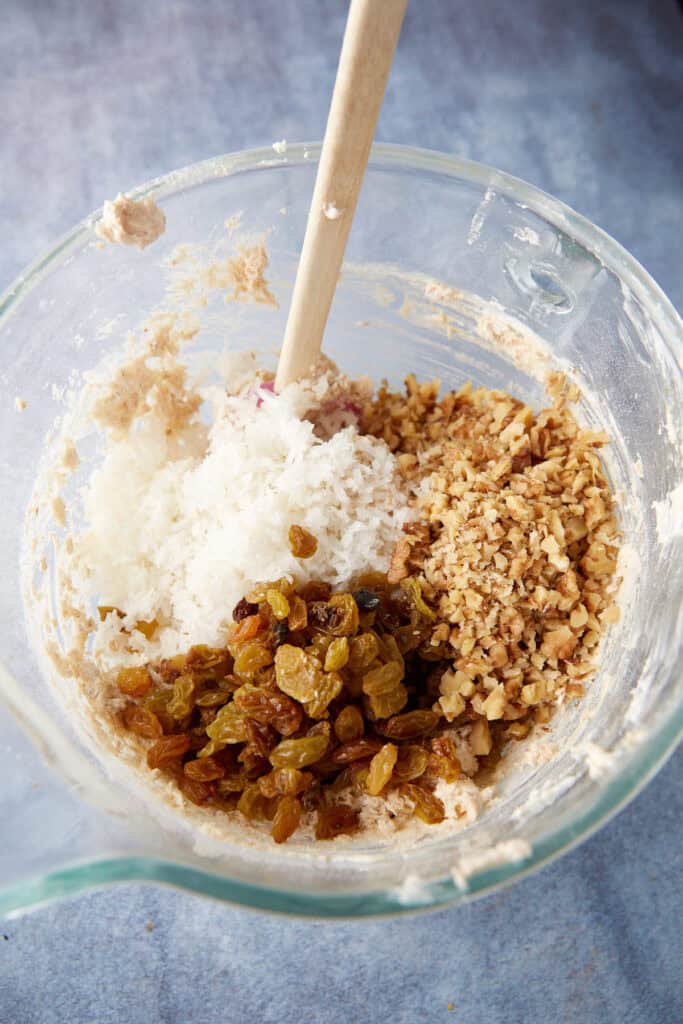 Coconut, raisins and walnuts added to a bowl of cookie dough.