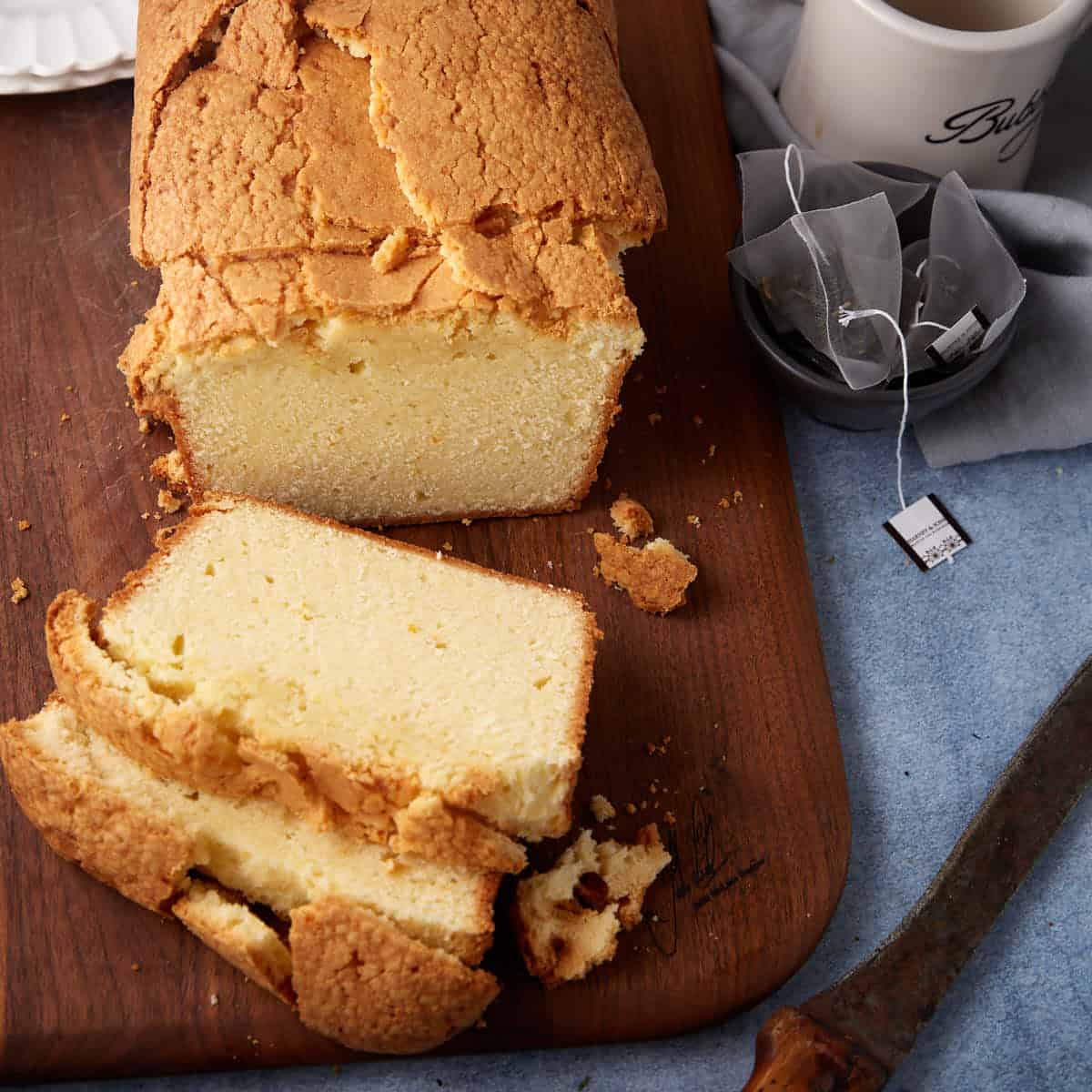 A sliced pound cake next to mugs.