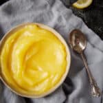 A bowl of lemon curd next to a spoon.