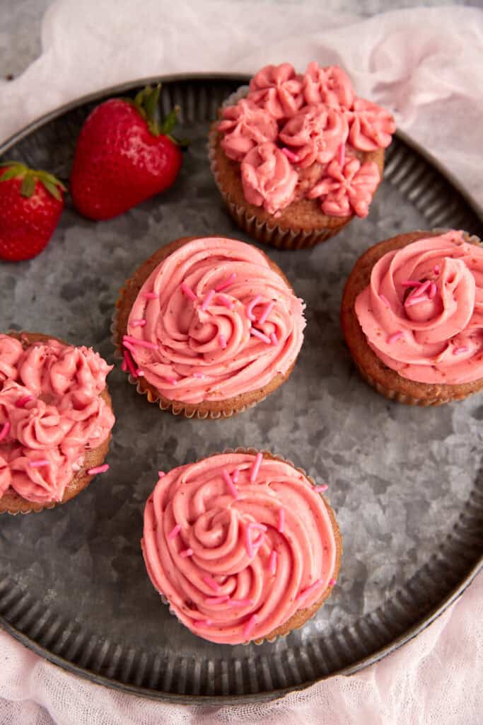 Strawberry frosting pipped onto cupcakes.